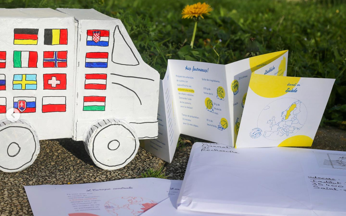 Le carnet Suède déplié dans l'herbe, devant une camionnette en carton couverte de drapeaux européens
